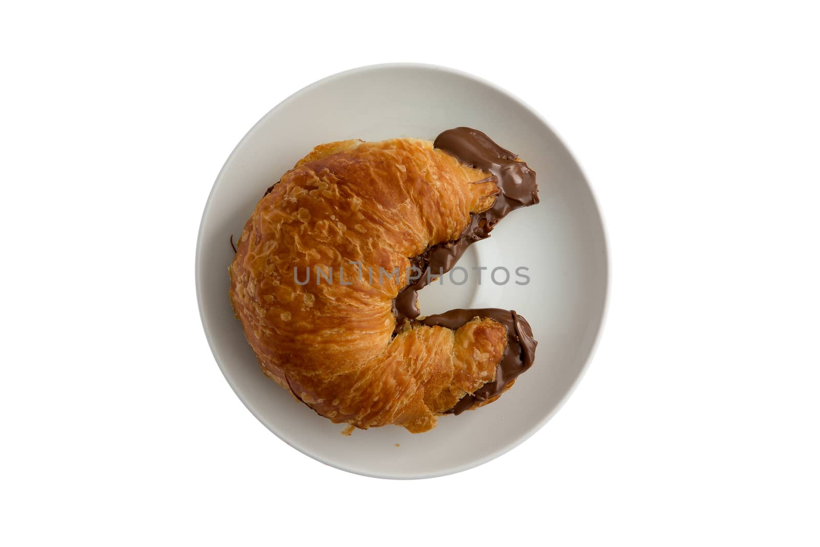 Freshly baked flaky buttery croissant filled to overflowing with hazelnut chocolate spread oozing onto the plate, tempting breakfast viewed from overhead isolated on white