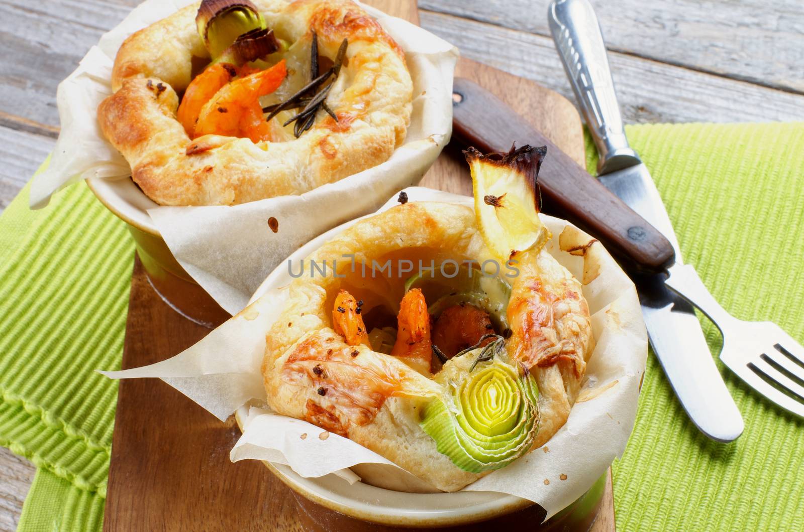 Two Ramekins with Puff Pastry Snacks with Shrimps, Leek and Cheese Oven-Baked on Wooden Cutting Board with Fork and Knife