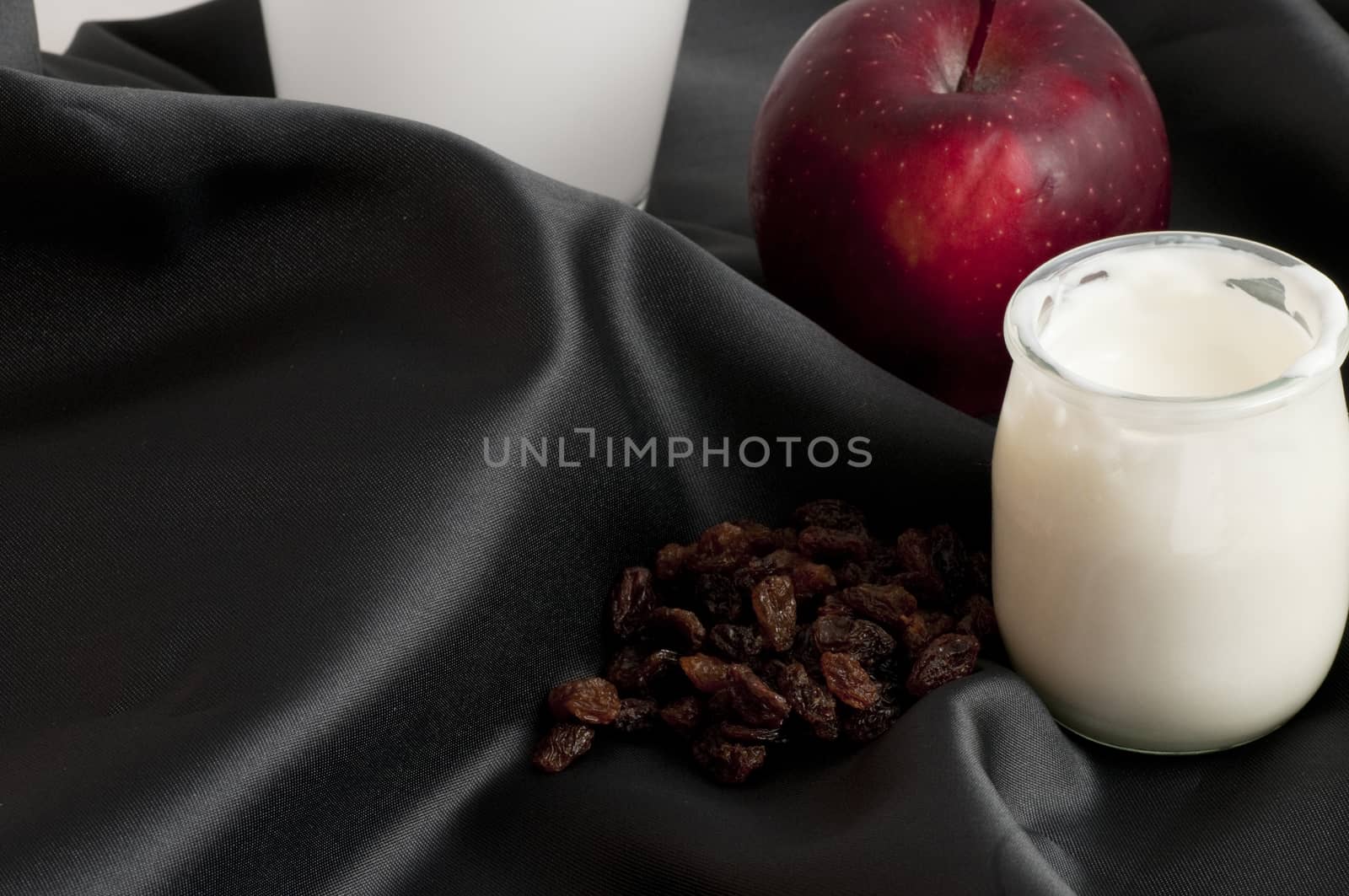 white yogurt in a bowl on a sheet of black silk with close blueberries and apple