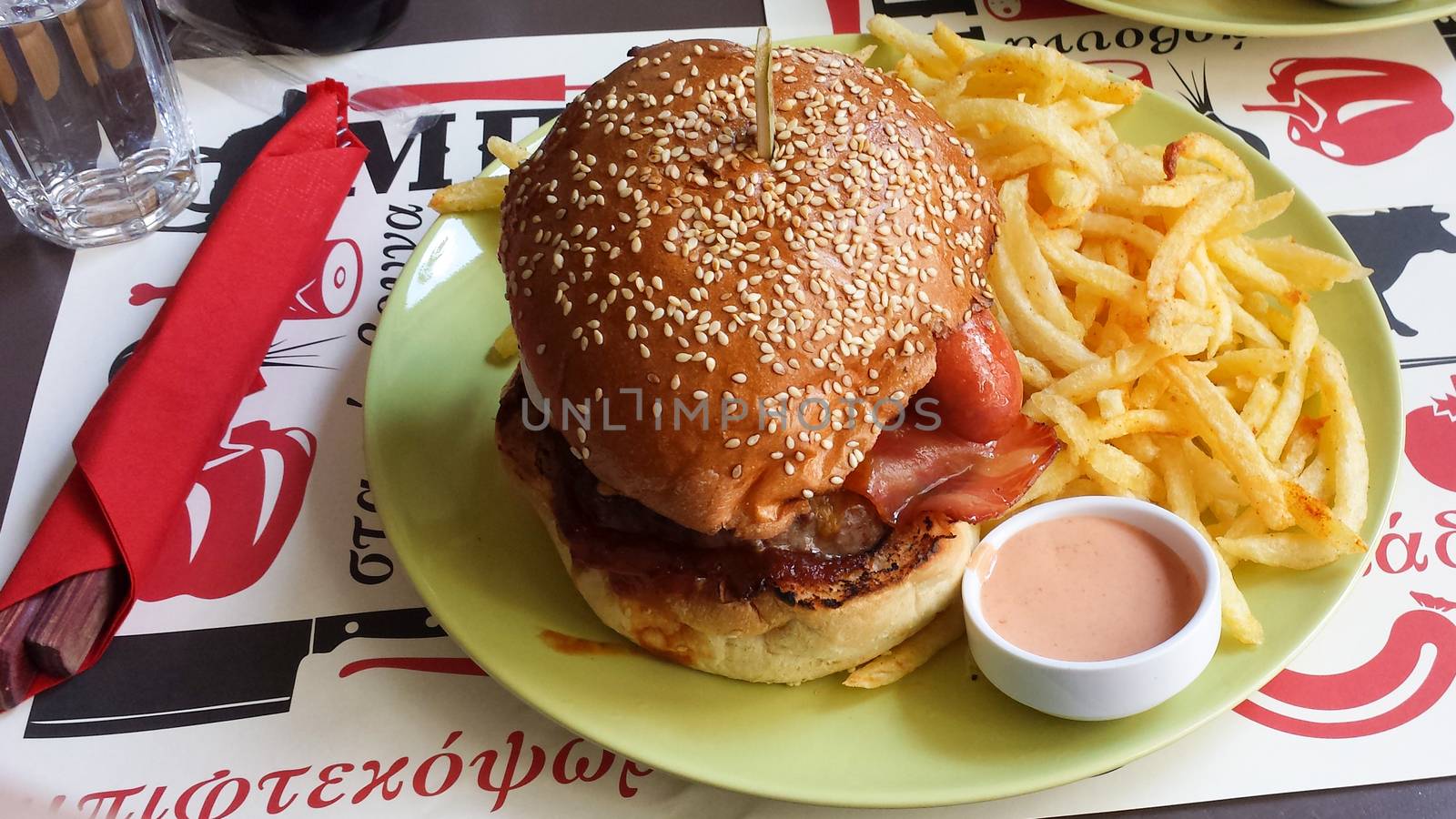 View of a huge hamburger with burger, fried eggs, sausage, barbeque sauce and bacon accompanied by fried potatoes and sauce.