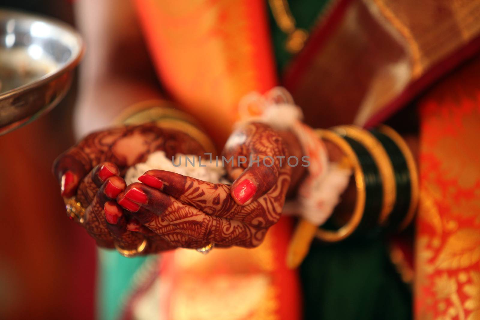 A bride's hand decorated with Mehendi/Henna holding holy food during a traditional Hindu wedding ritual.