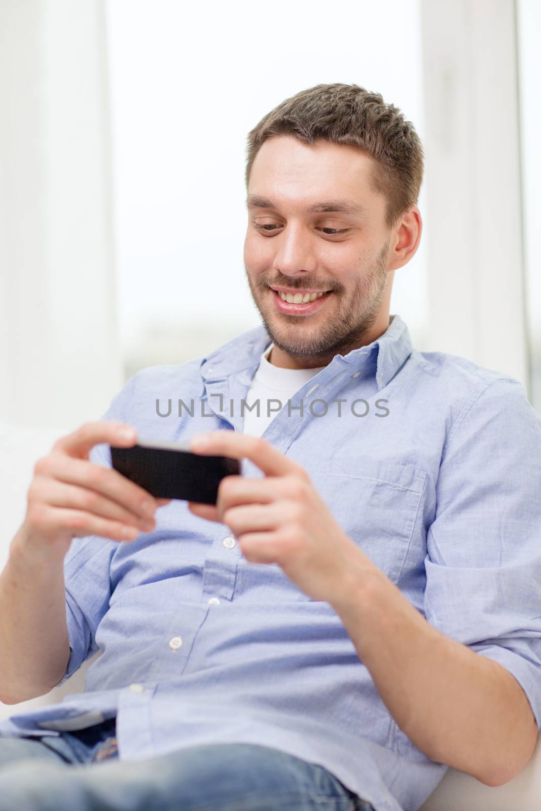 smiling man with smartphone at home by dolgachov