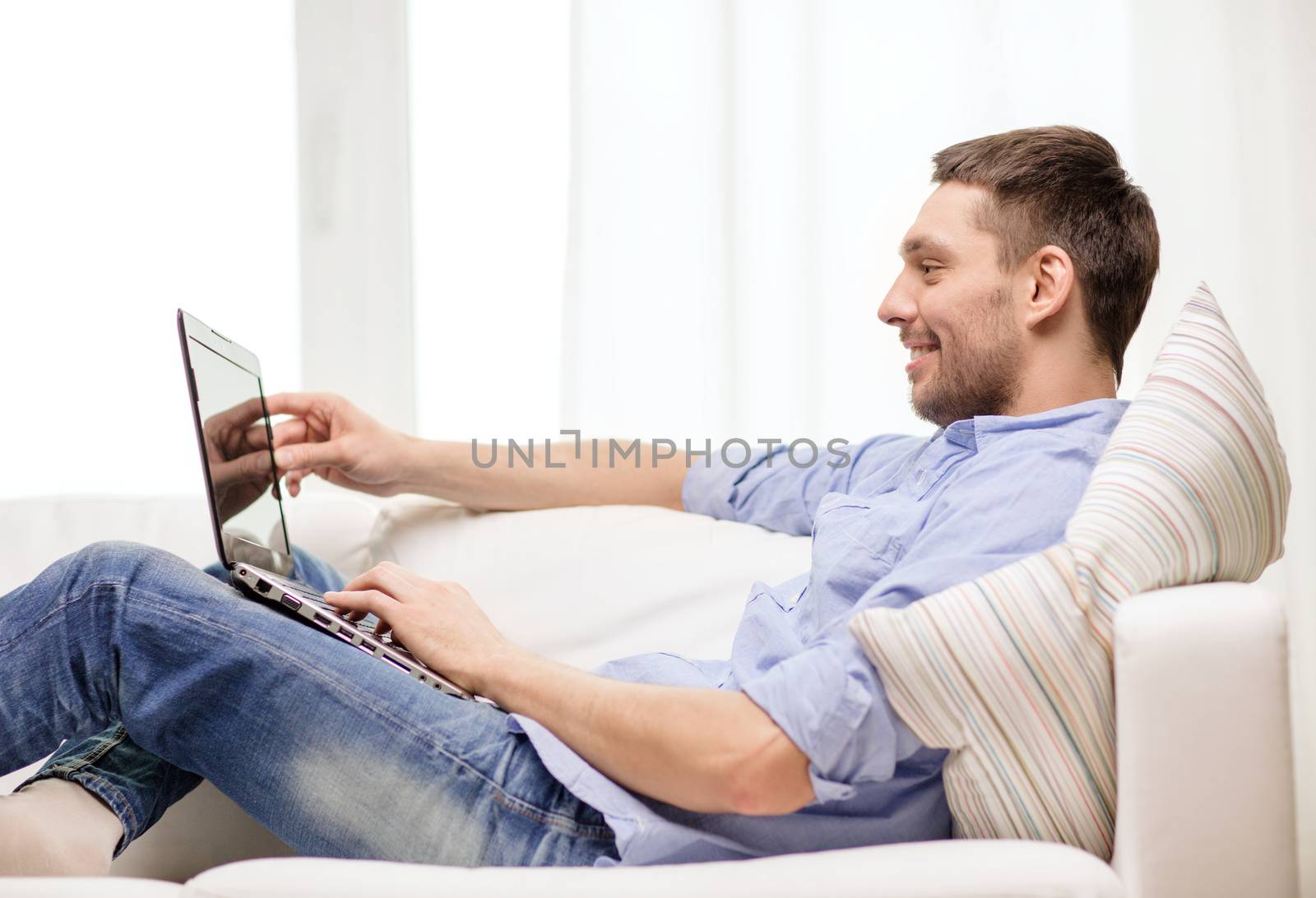 smiling man working with laptop at home by dolgachov