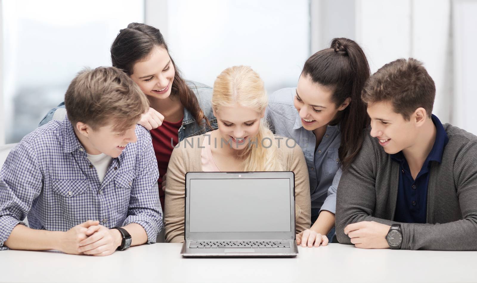 smiling students looking at blank lapotop screen by dolgachov