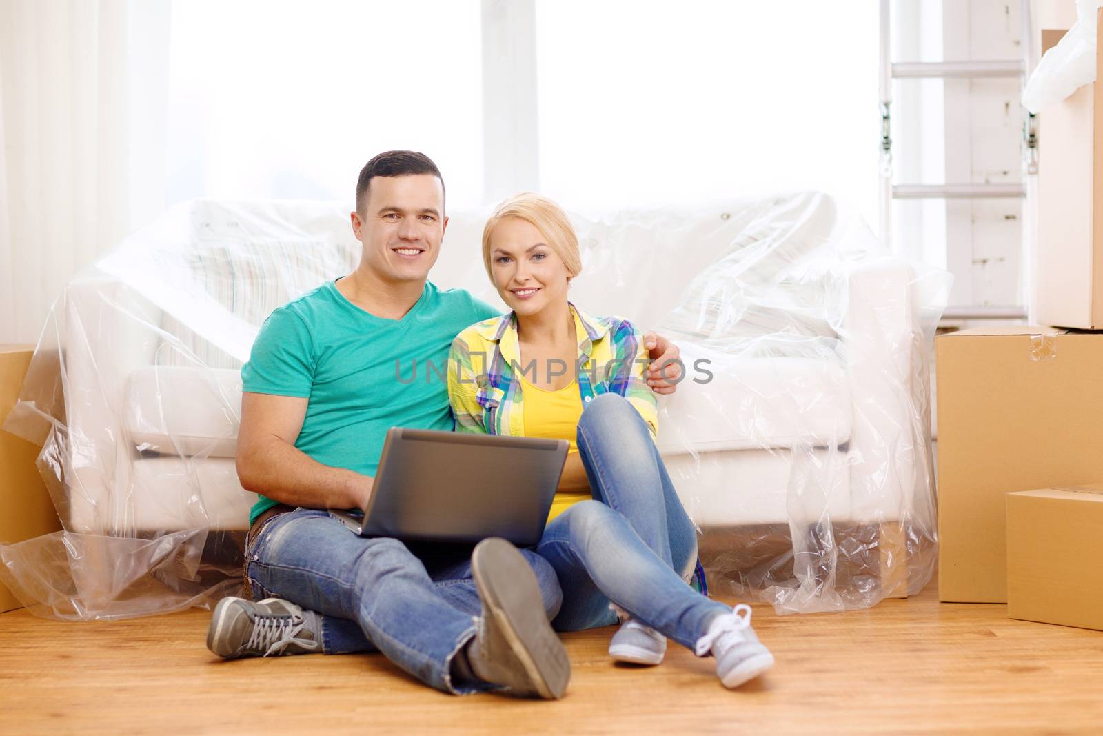 couple with laptop sitting on floor in new house by dolgachov