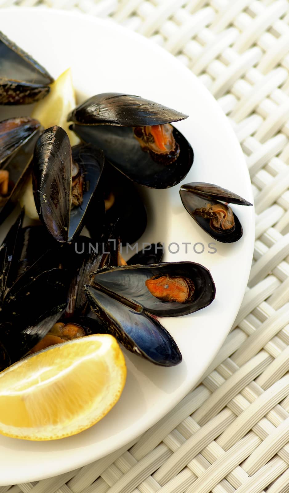 Arrangement of Boiled Mussels with Lemon on White Plate closeup on Wicker background. Top View