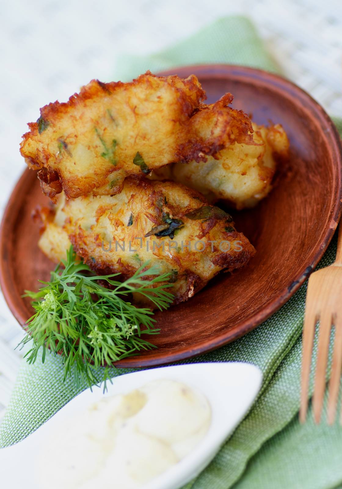 Delicious Breaded Fish Cutlets with Garlic, Greens and Tartar Sauce on Brown Plate with Wooden Fork closeup on Green Napkin. Selective Focus