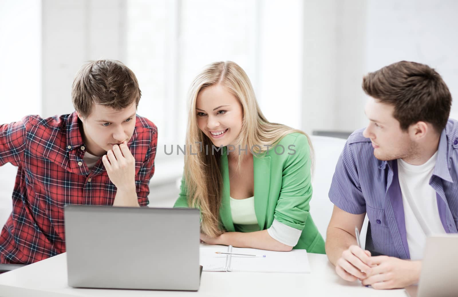 smiling students looking at laptop at school by dolgachov