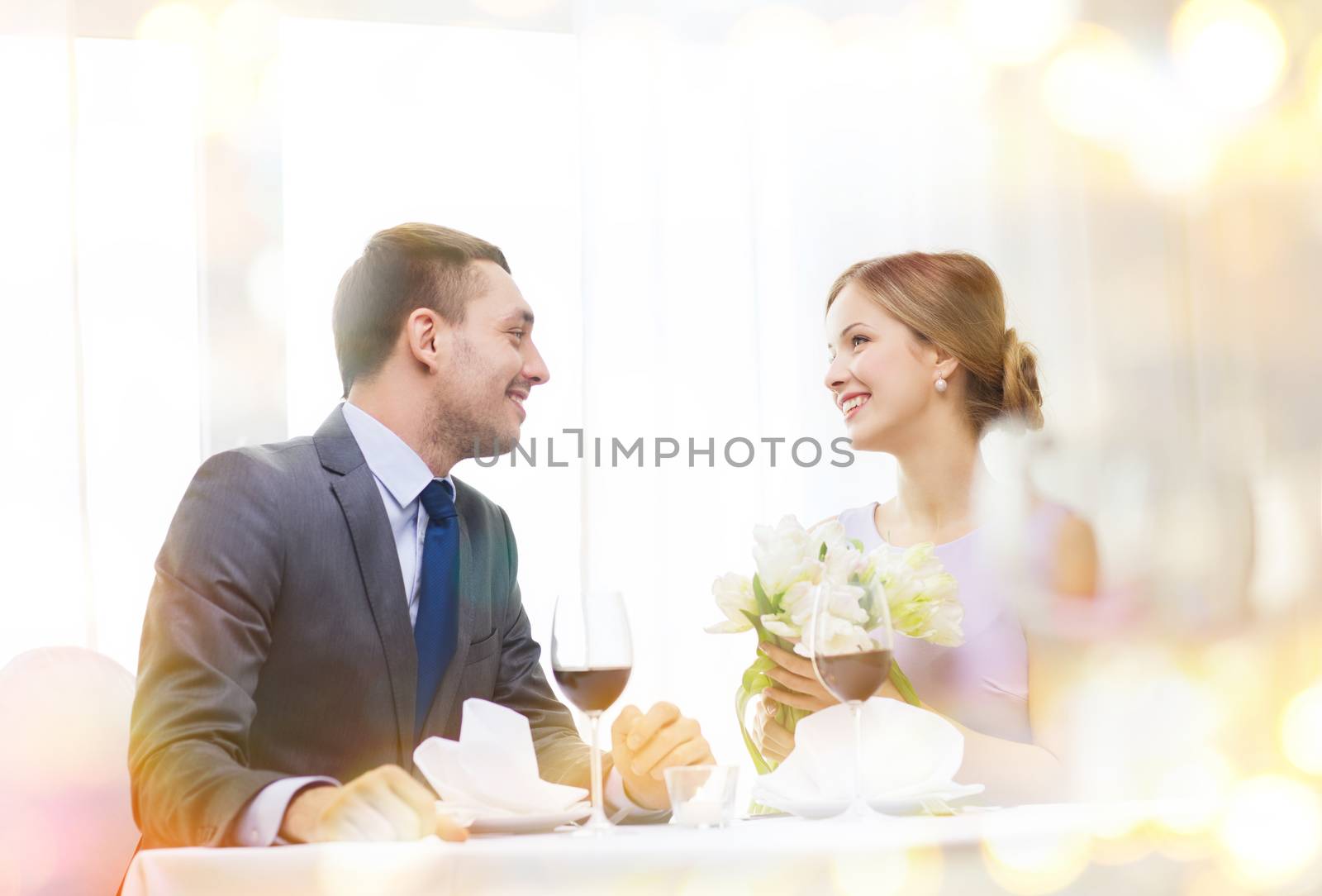 restaurant, couple and holiday concept - smiling man giving girlfriend or wife bouquet of flowers at restaurant