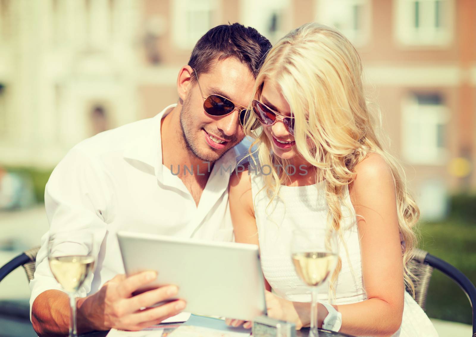 summer holidays, dating and technology concept - couple looking at tablet pc in cafe in the city