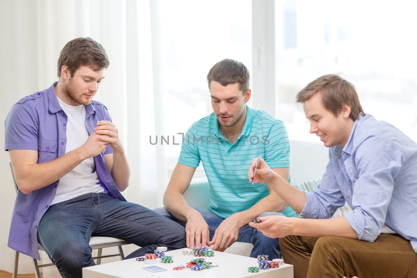 leisure, games and lifestyle concept - happy three male friends playing poker at home