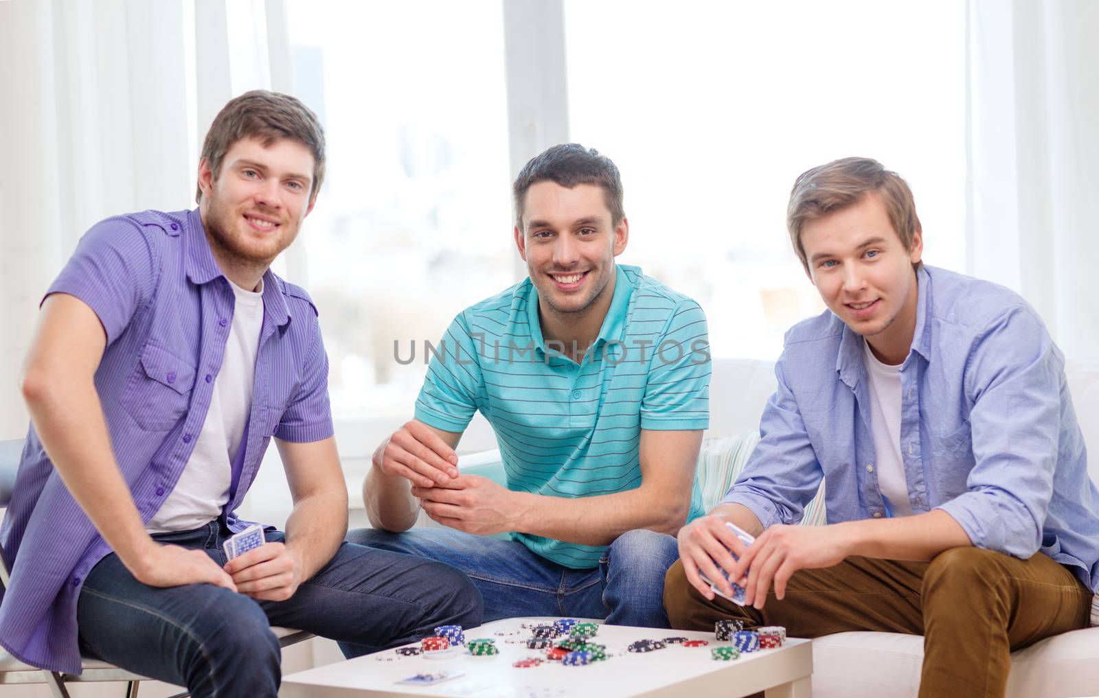 leisure, games and lifestyle concept - happy three male friends playing poker at home