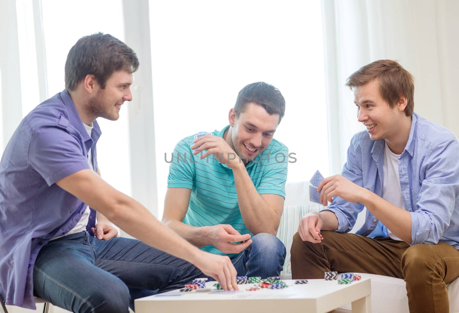 leisure, games and lifestyle concept - happy three male friends playing poker at home