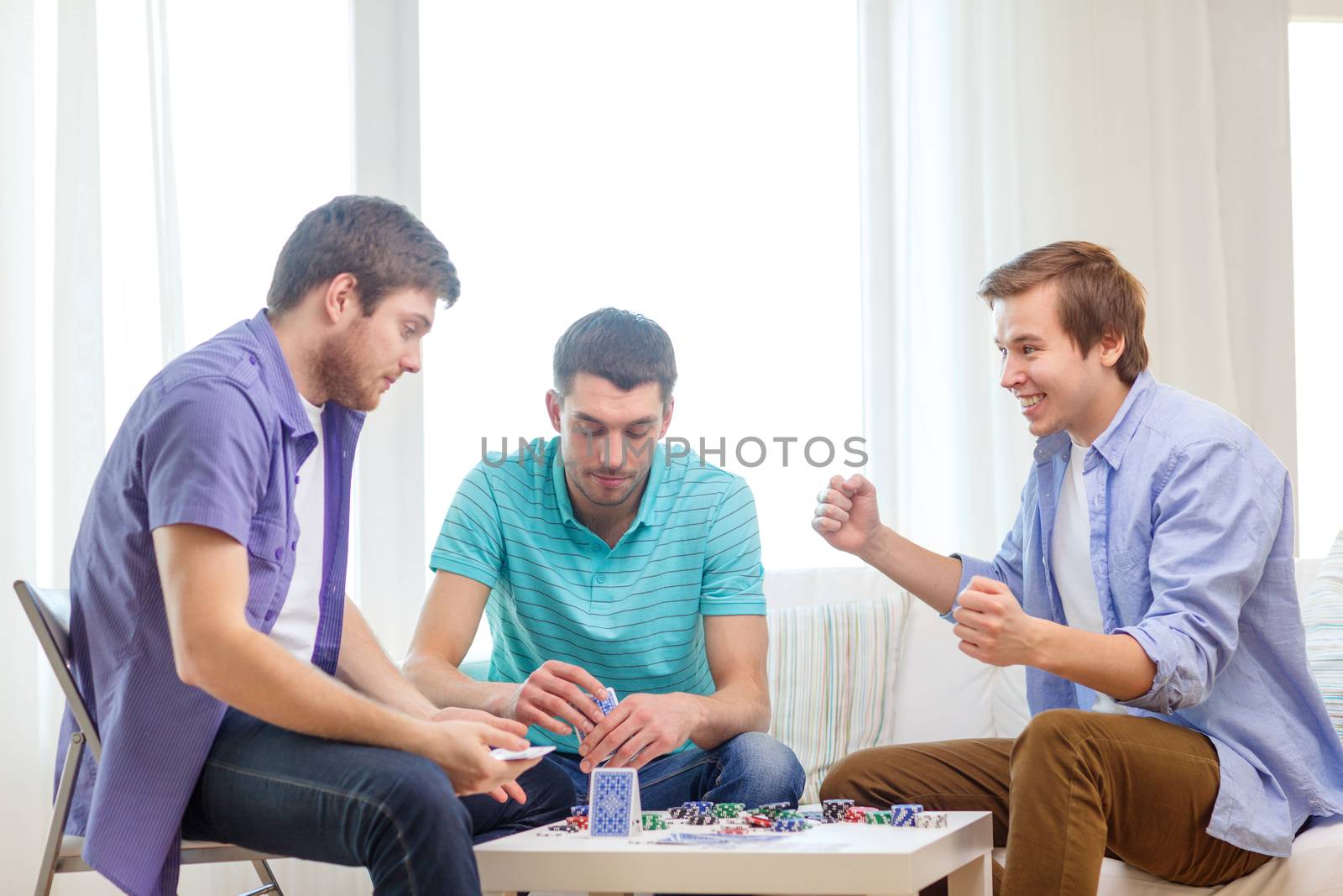 leisure, games and lifestyle concept - happy three male friends playing poker at home