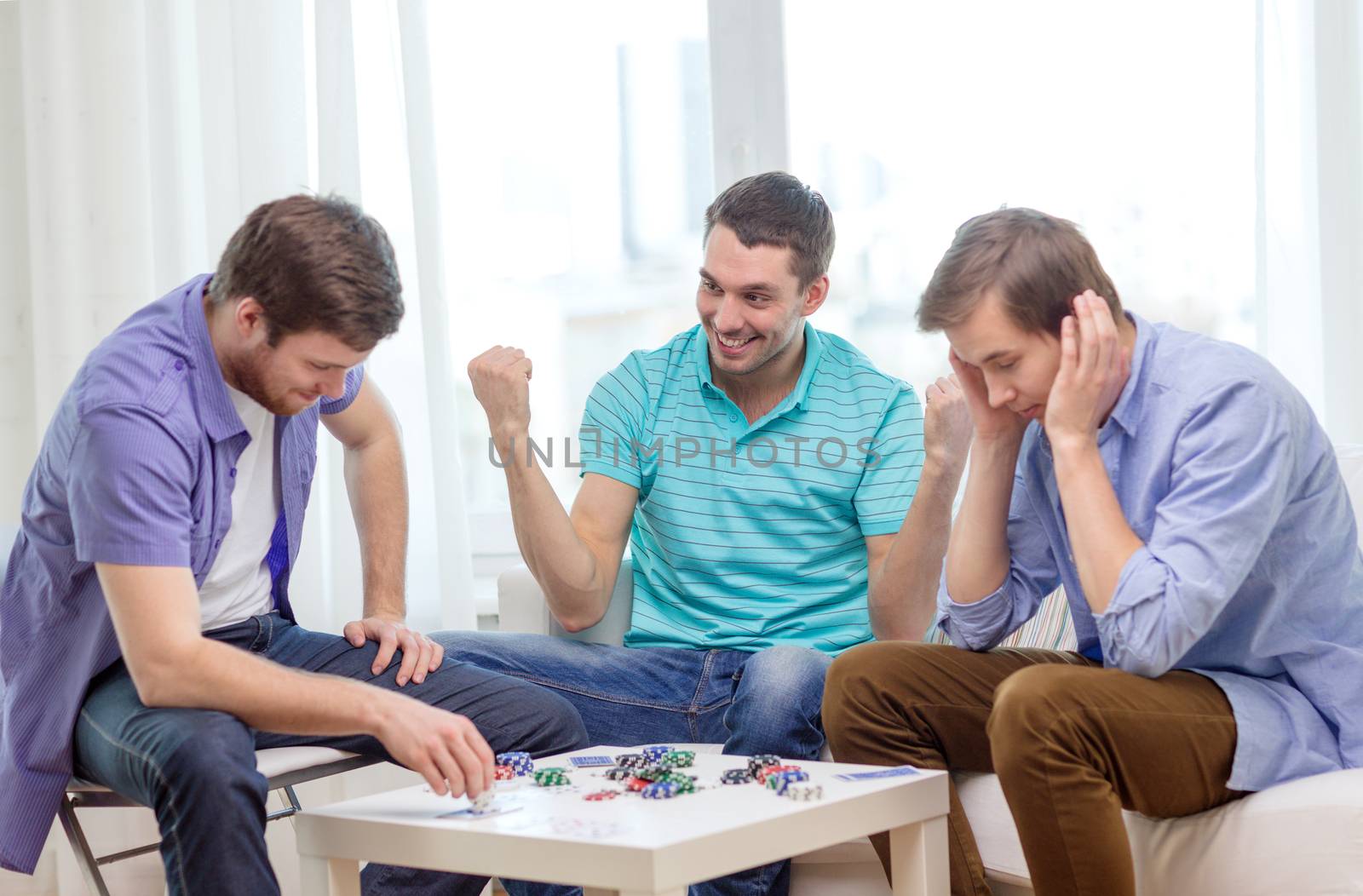 happy three male friends playing poker at home by dolgachov