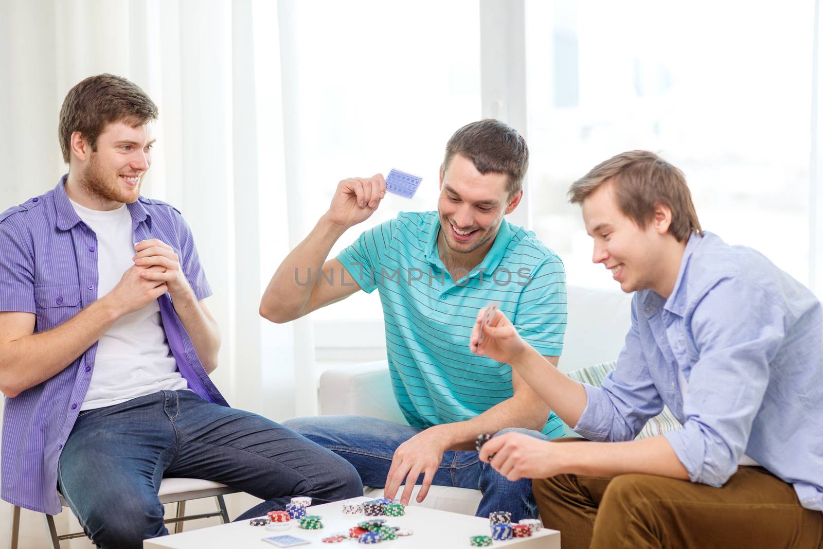 happy three male friends playing poker at home by dolgachov