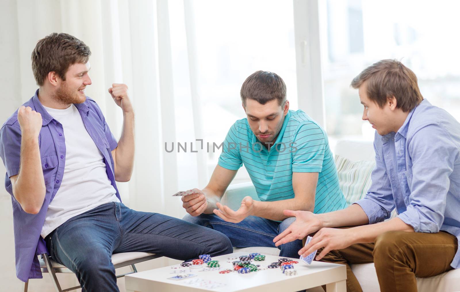 leisure, games and lifestyle concept - happy three male friends playing poker at home