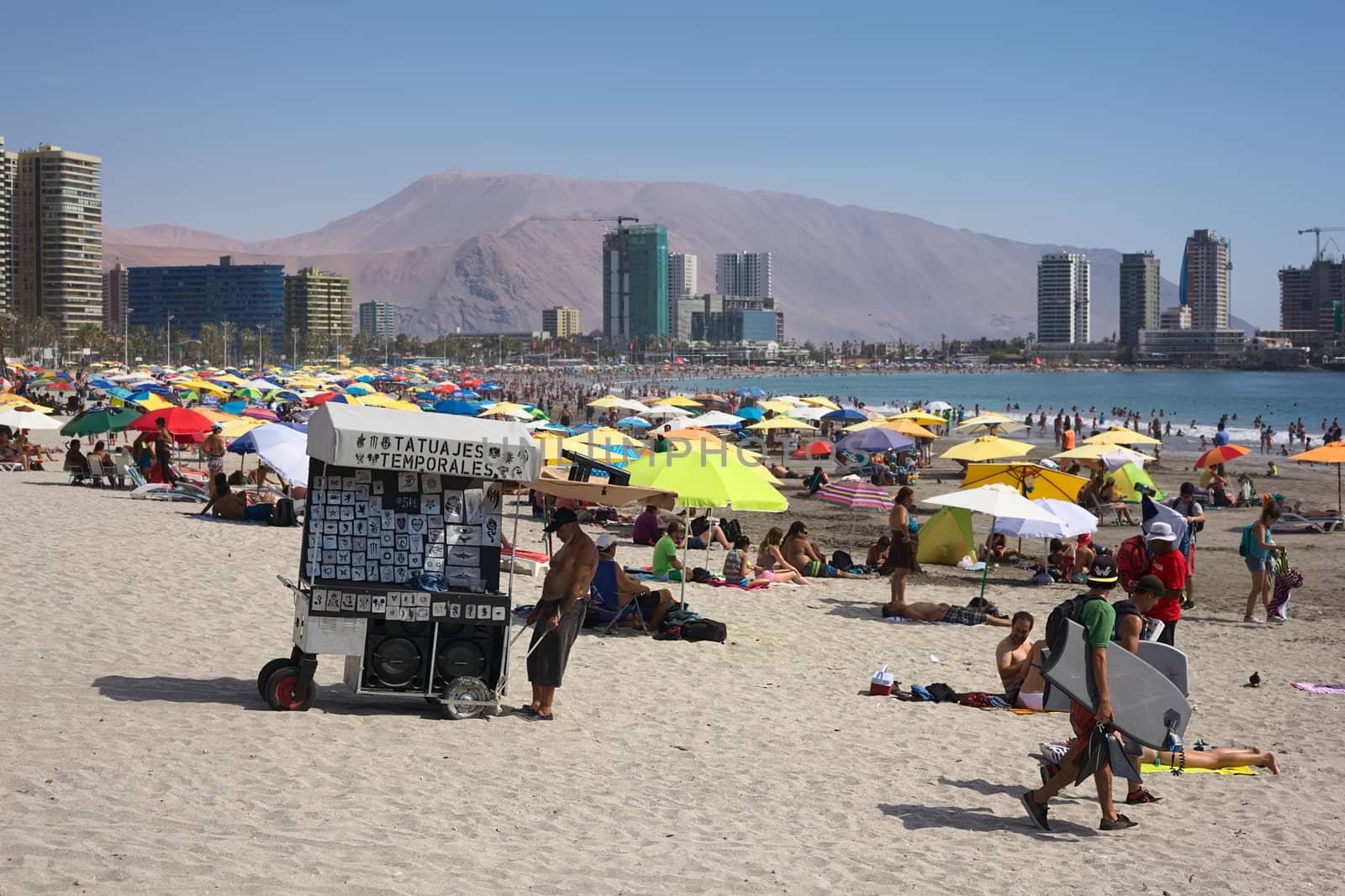 IQUIQUE, CHILE - JANUARY 23, 2015: Unidentified man pulling a cart through the sand offering temporal tattoos on the crowded Cavancha beach on January 23, 2015 in Iquique, Chile. Iquique is a popular beach town and free port city in Northern Chile.  