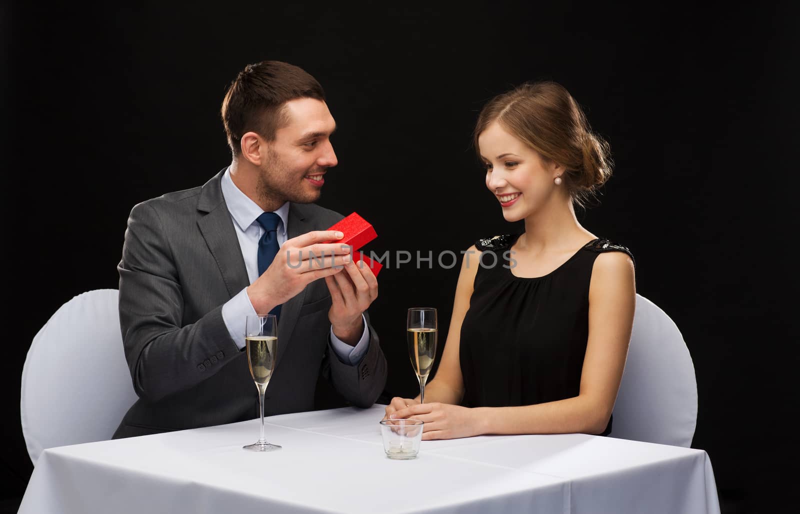 restaurant, couple and holiday concept - excited young woman looking at boyfriend with gift box at restaurant