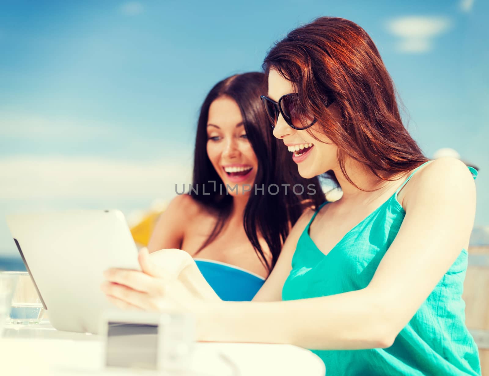 summer holidays, vacation and technology - girls looking at tablet pc in cafe on the beach