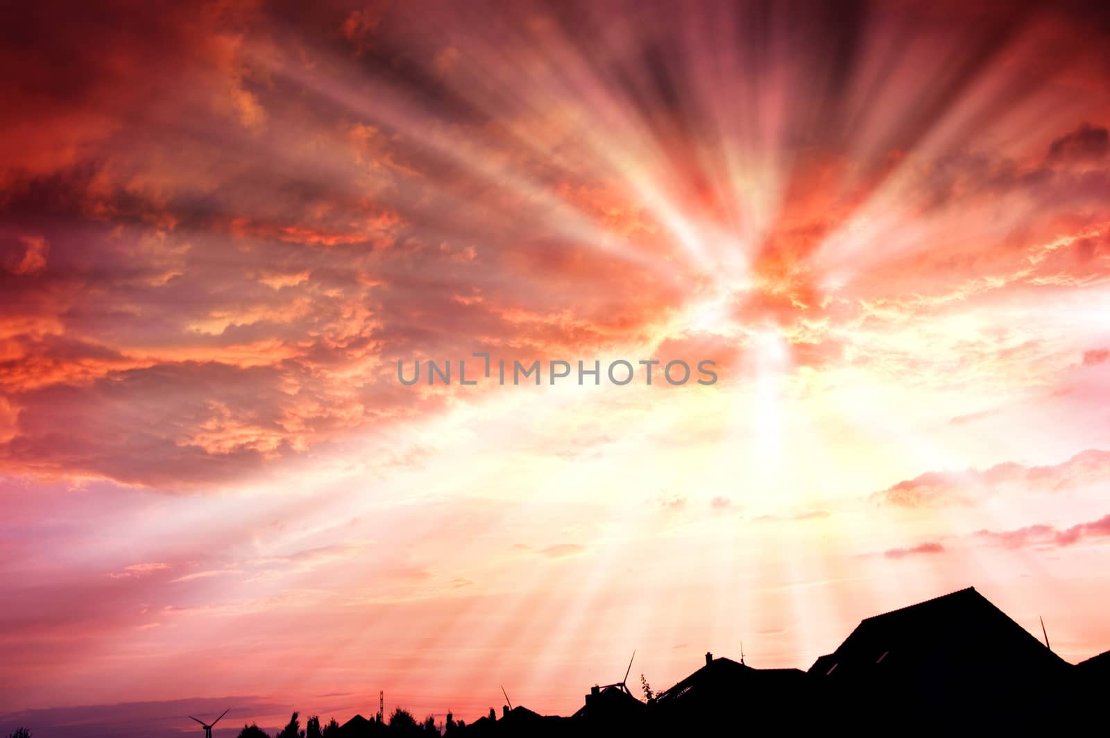 Sunset red sky with beams and dark dramatic clouds over houses.