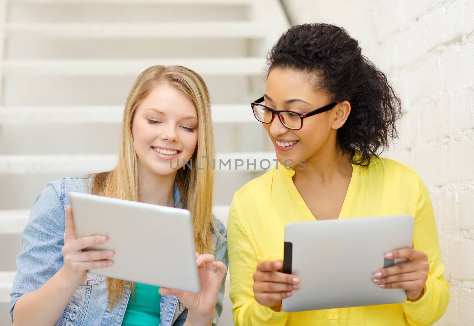 education and technology concept - smiling female students with tablet pc computer sitting on staircase