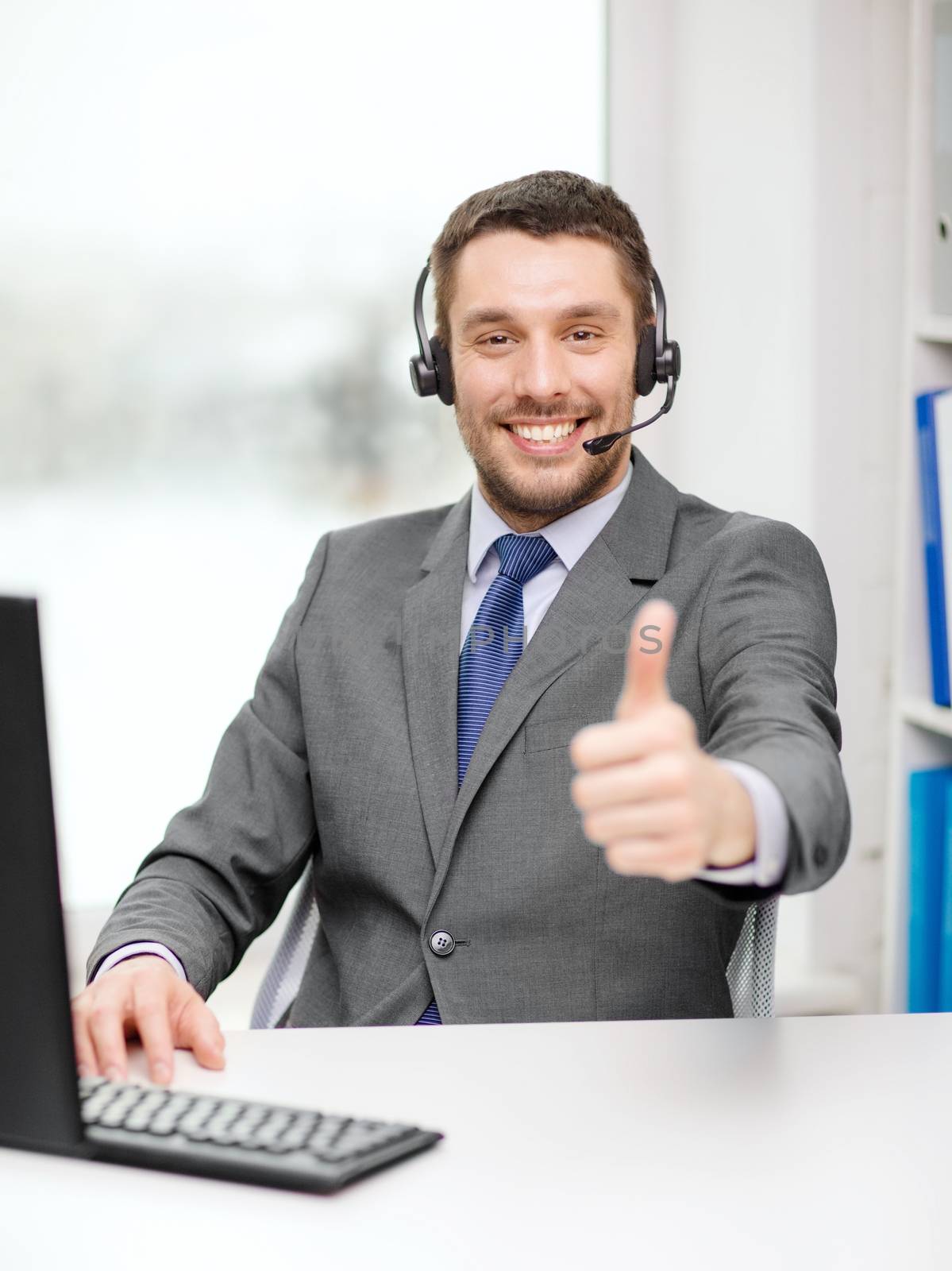 business, communication and technology concept - friendly male helpline operator with headphones and computer at call center showing thumbs up