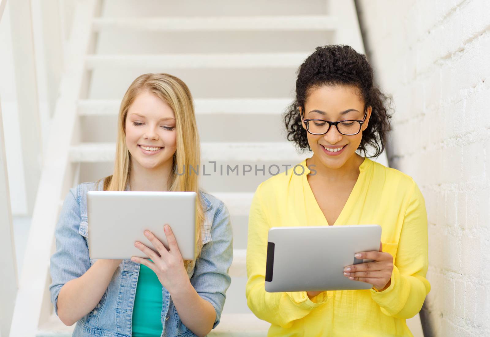 education and technology concept - smiling female students with tablet pc computer sitting on staircase