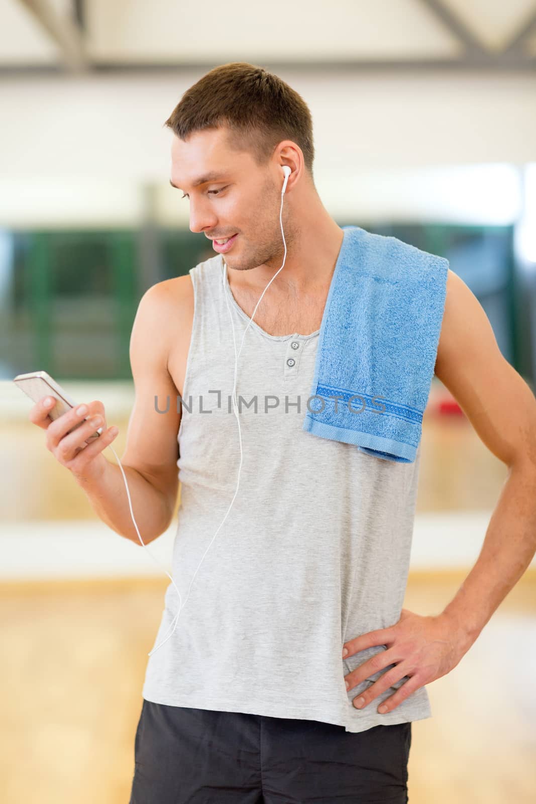 fitness, sport, training, gym, technology and lifestyle concept - young man with smartphone and towel in gym