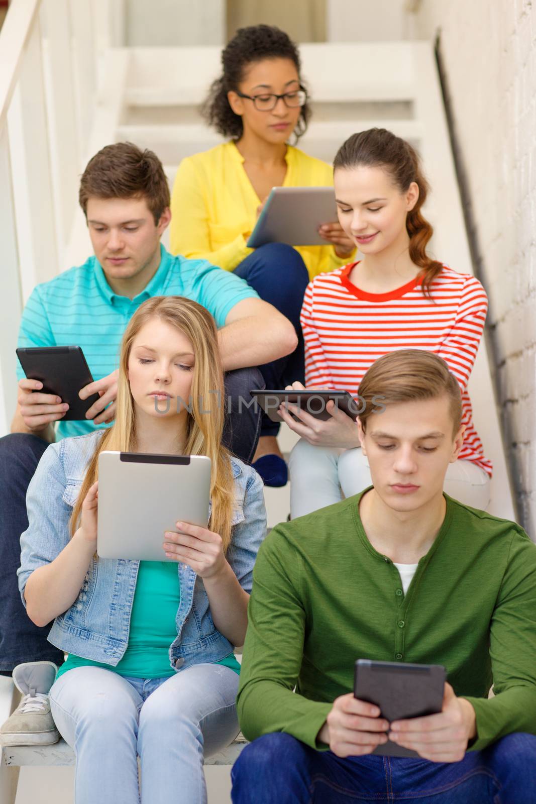 education and technology concept - busy students with tablet pc computer sitting on staircase