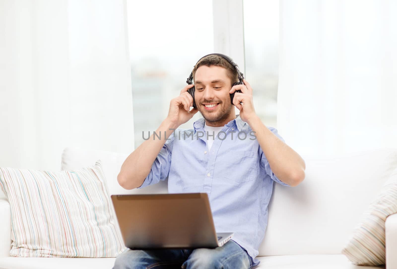 technology, home, music and lifestyle concept - smiling man with laptop and headphones at home