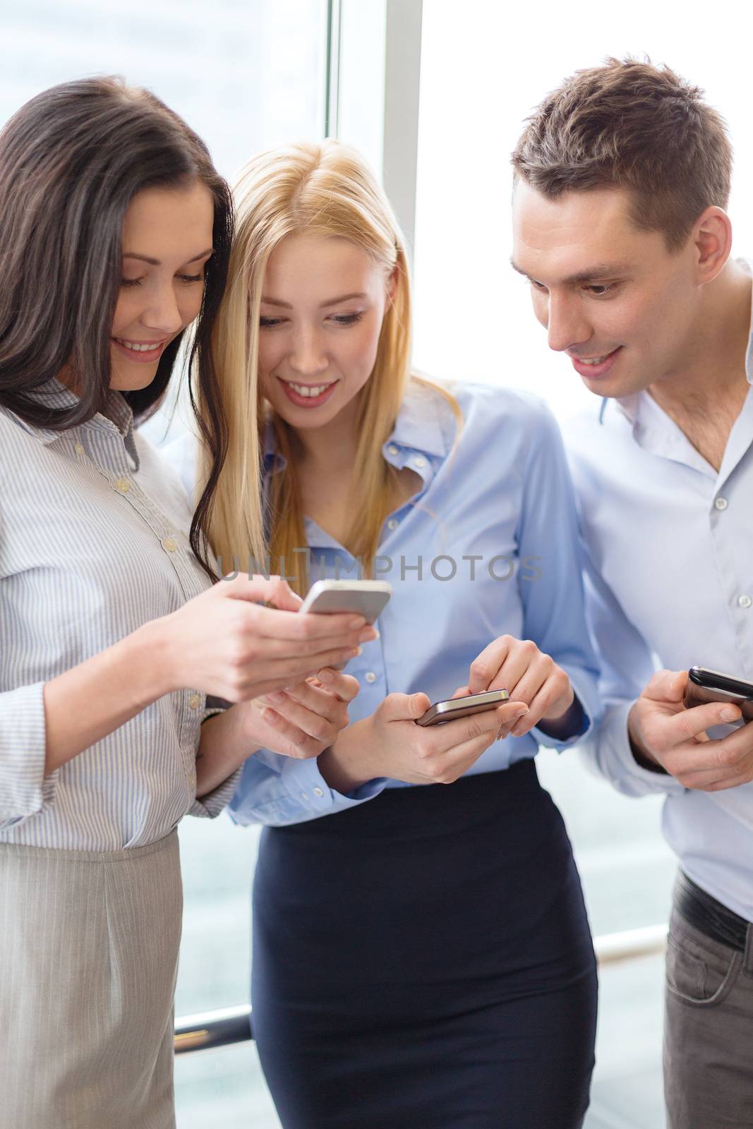 smiling business team with smartphones in office by dolgachov