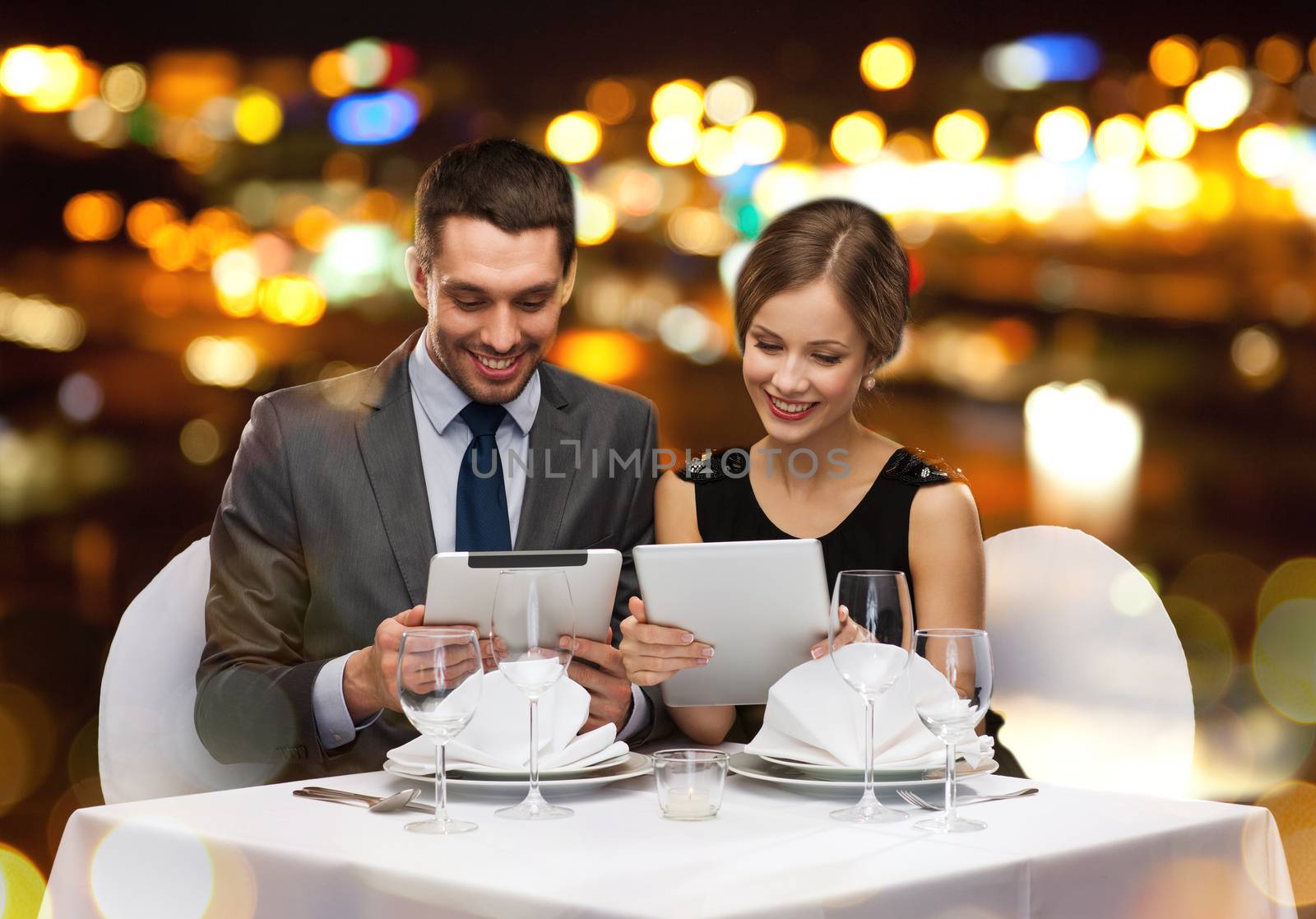 restaurant, couple, technology and holiday concept - smiling couple with menus on tablet pc computers at restaurant