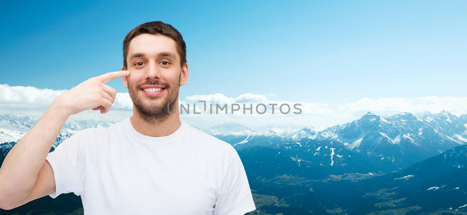 smiling young handsome man pointing to eyes by dolgachov