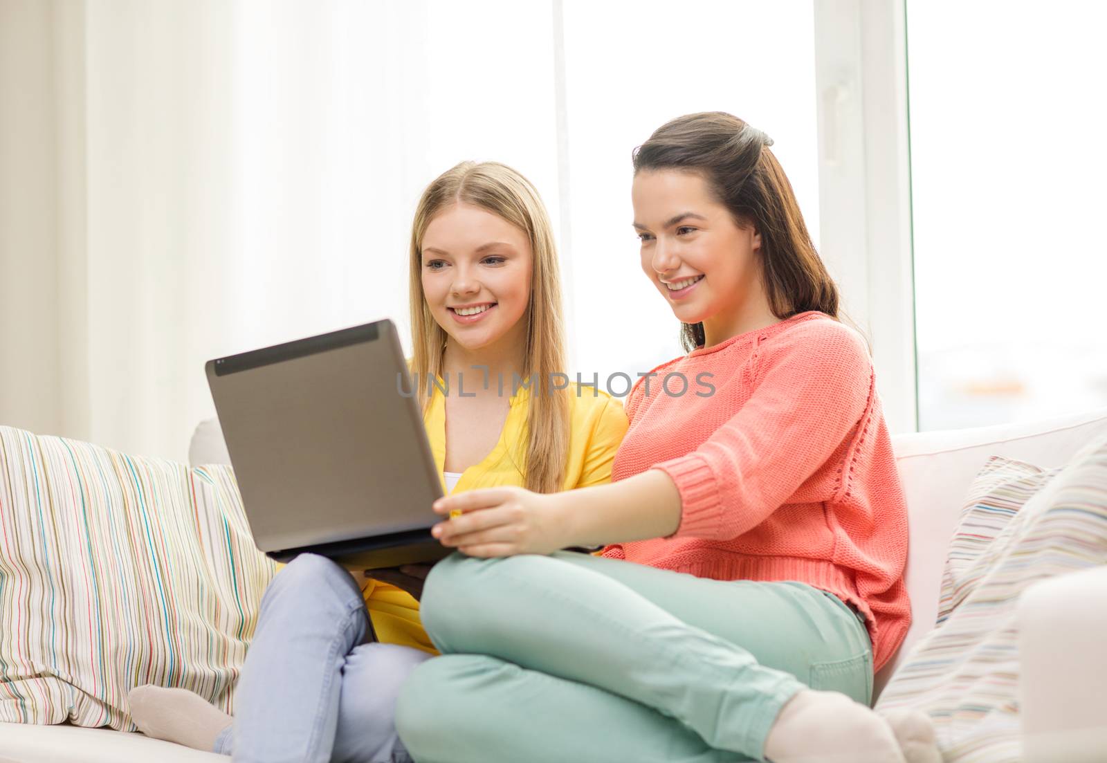 friendship, technology and internet concept - two smiling teenage girls with laptop computer at home