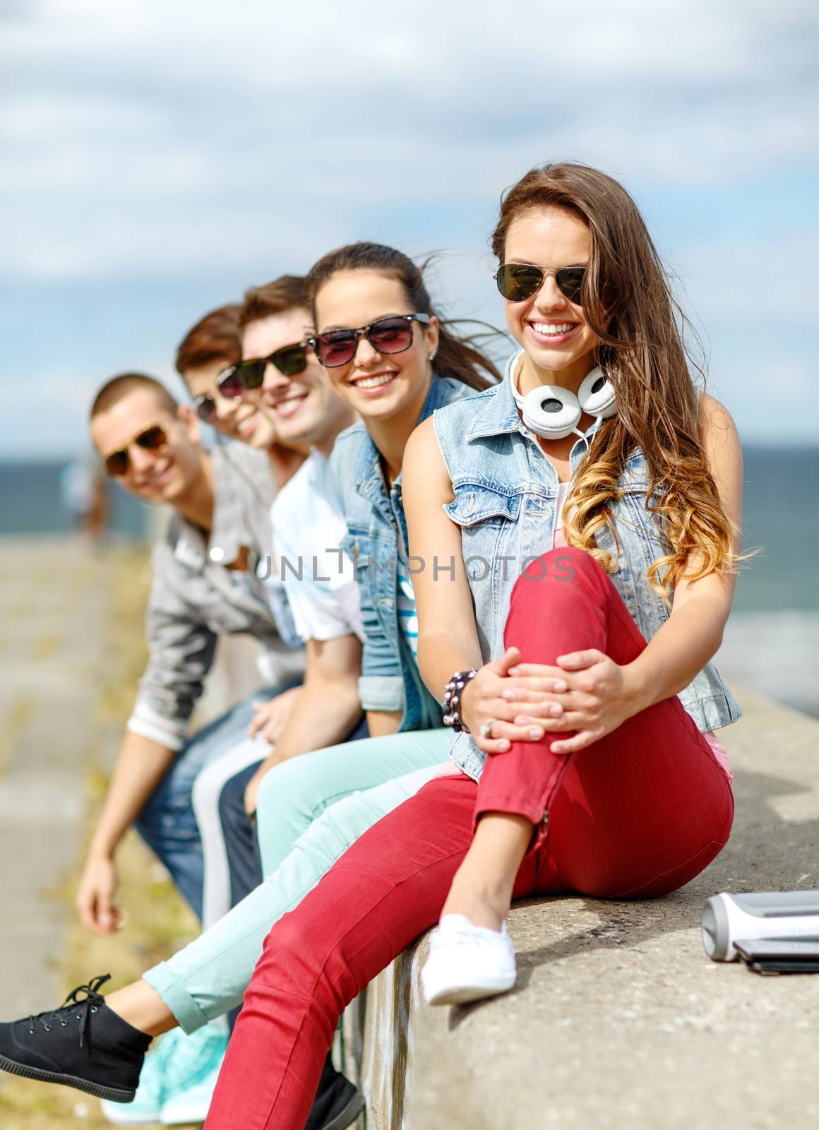 summer holidays and teenage concept - smiling teenage girl in sunglasses hanging out with friends outdoors