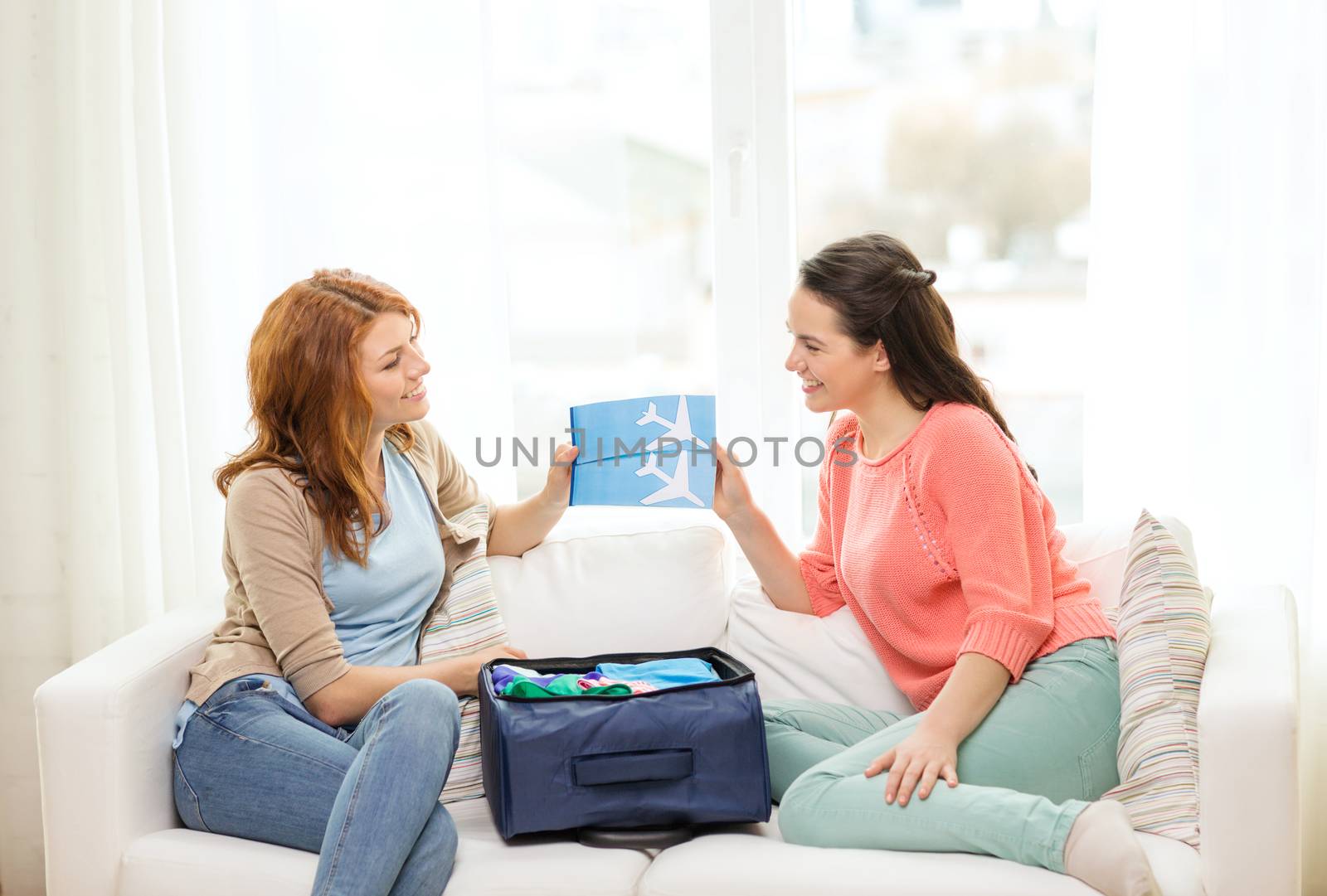 travel, vacation and friendship concept - two smiling teenage girls with plane tickets and packed suitcase