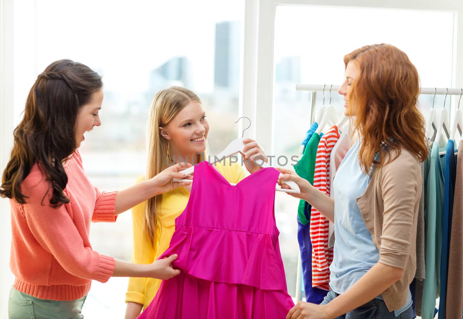 shopping, fashion and friendship concept - three smiling friends trying on some clothes at home or shopping mall