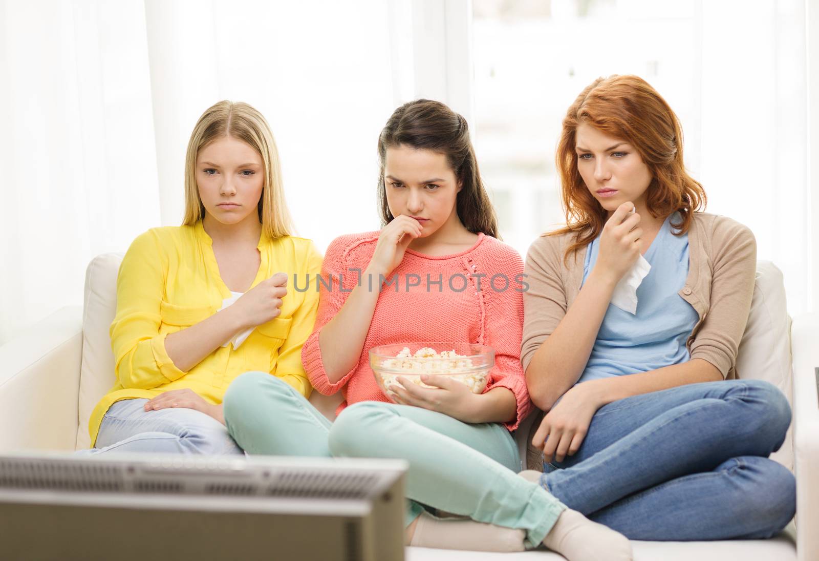 home, technology and friendship concept - three sad teenage girl watching tv at home and eating popcorn