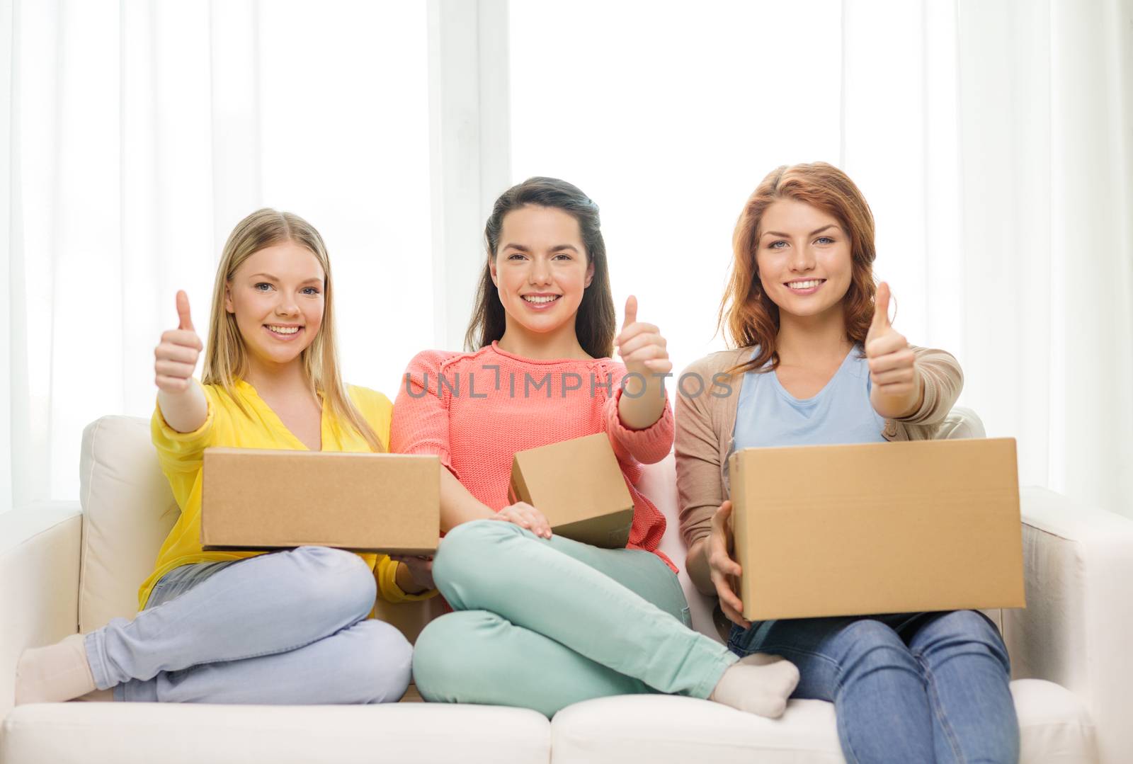 transportation, post and friendship concept - three smiling teenage girls with cardboard boxes at home showing thumbs up