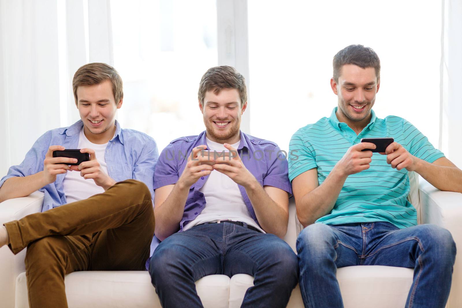 smiling friends with smartphones at home by dolgachov