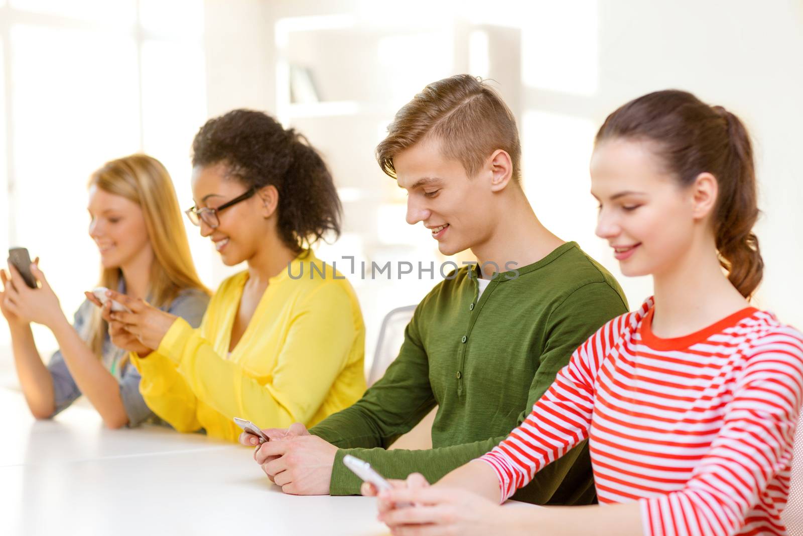 four smiling students with smartphones at school by dolgachov