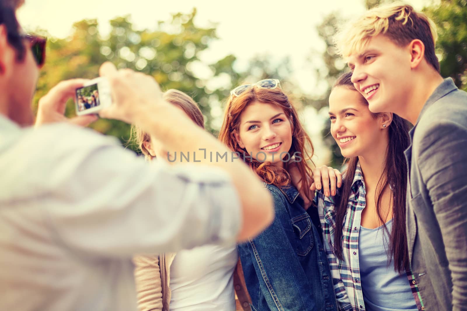 summer holidays, electronics and teenage concept - group of smiling teenagers taking photo with digital camera outside