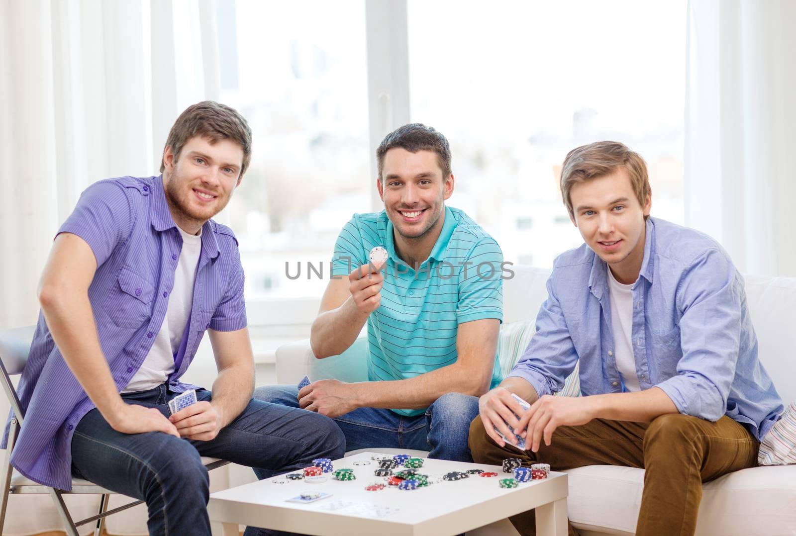 happy three male friends playing poker at home by dolgachov