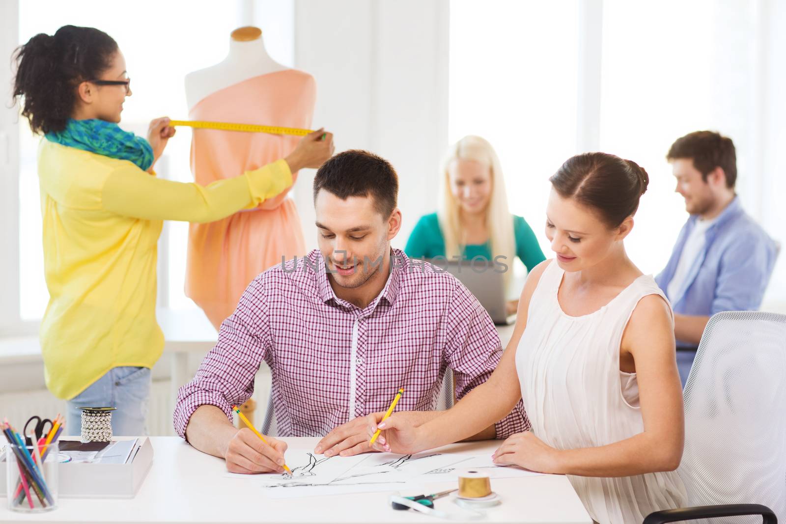 startup, education, fashion and office concept - smiling designers drawing sketches and adjusting dress on mannequin in office