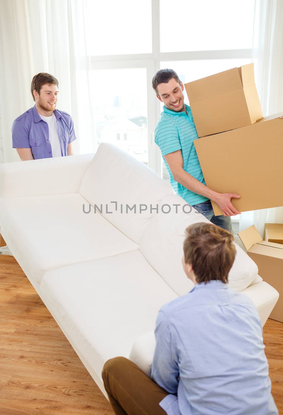 moving, real estate and friendship concept - smiling male friends with sofa and boxes at new home