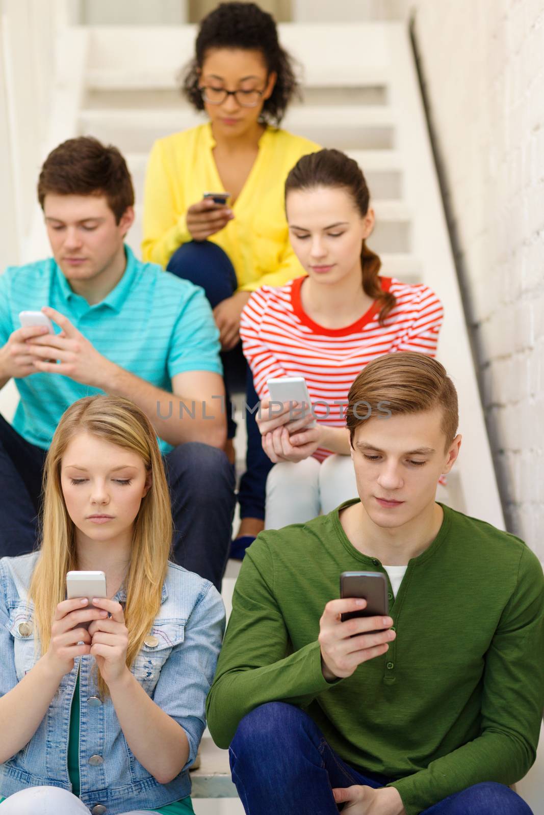 education, leisure and technology concept - busy students with smartphones sitting on staircase