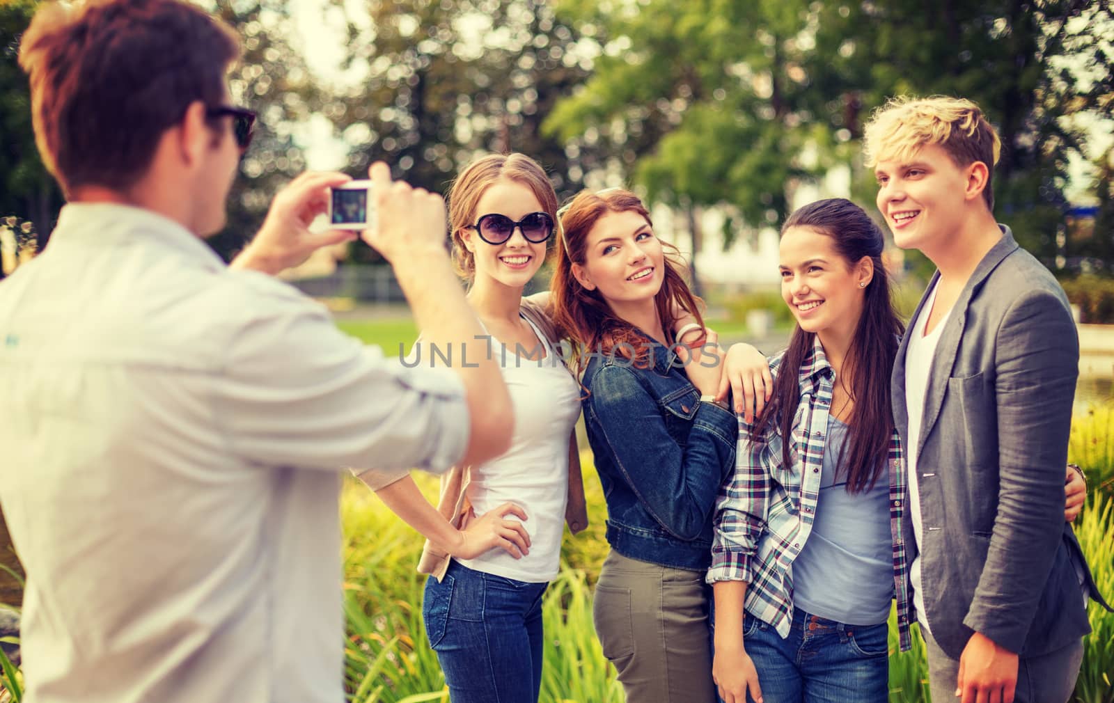 summer holidays, electronics and teenage concept - group of smiling teenagers taking photo with digital camera outside