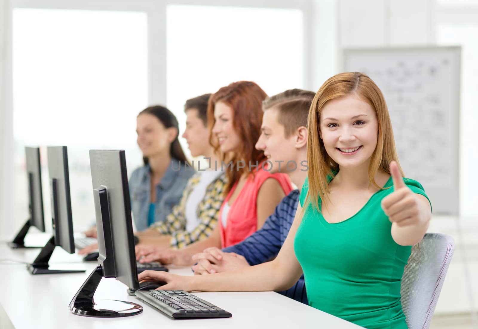 education, technology and school concept - smiling female student with classmates in computer class at school showing thumbs up