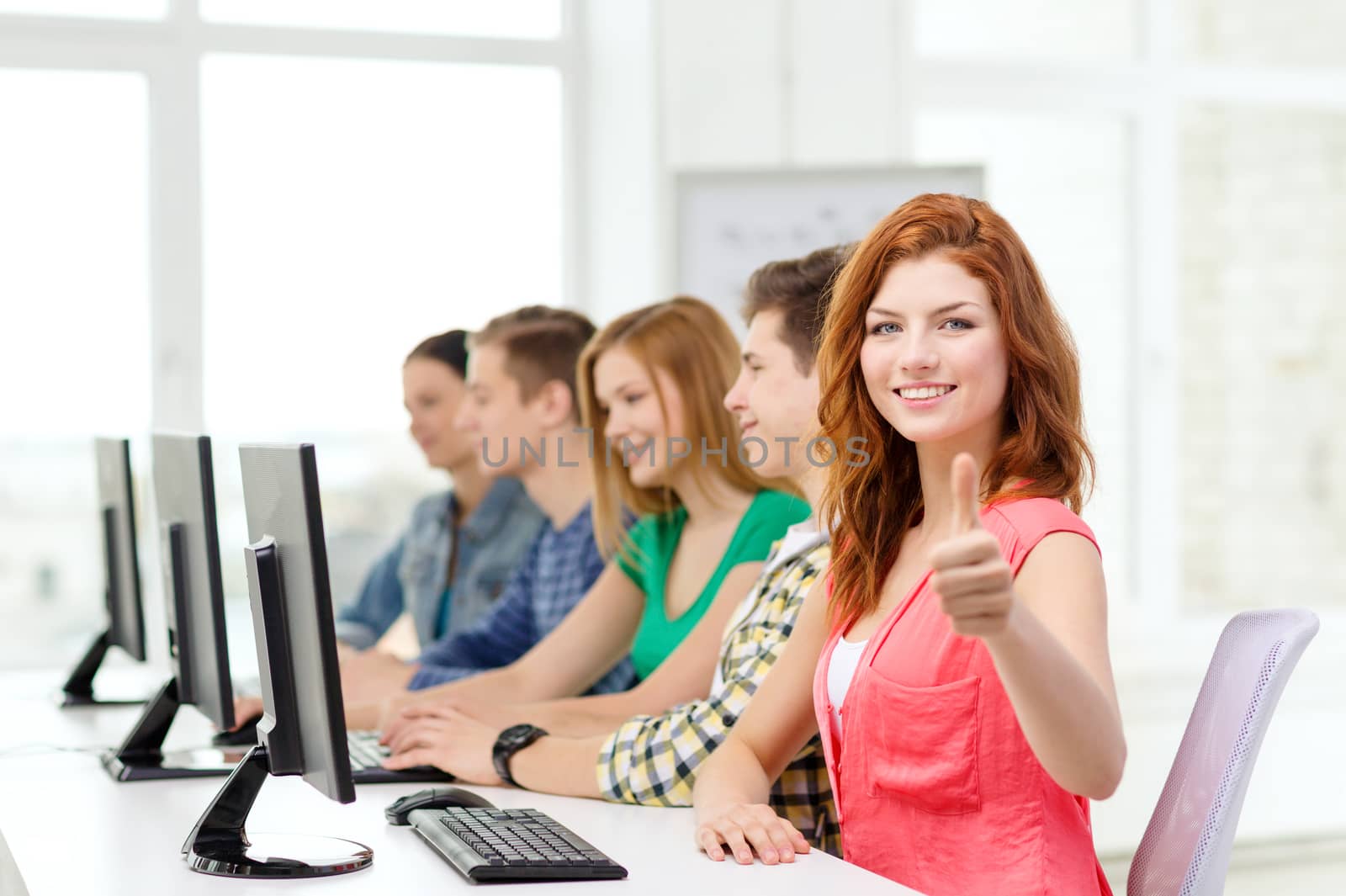 education, technology and school concept - smiling female student with classmates in computer class at school showing thumbs up